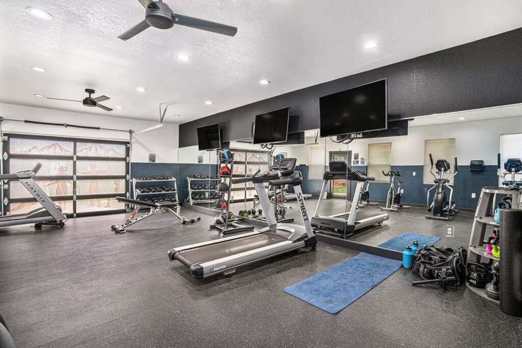 Fitness center with yoga and cardio equipment facing a large wall mirror with televisions overhead