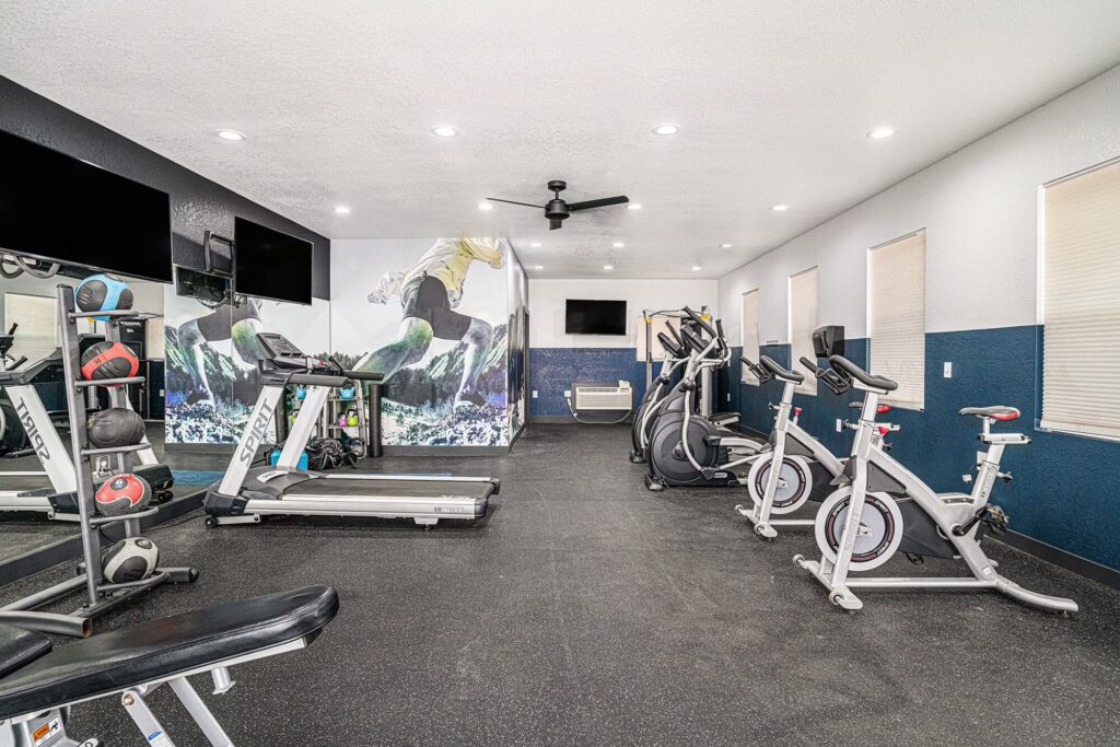 Fitness center with cardio equipment, overhead fans, a large mirror on the wall, and a colorful athletic mural